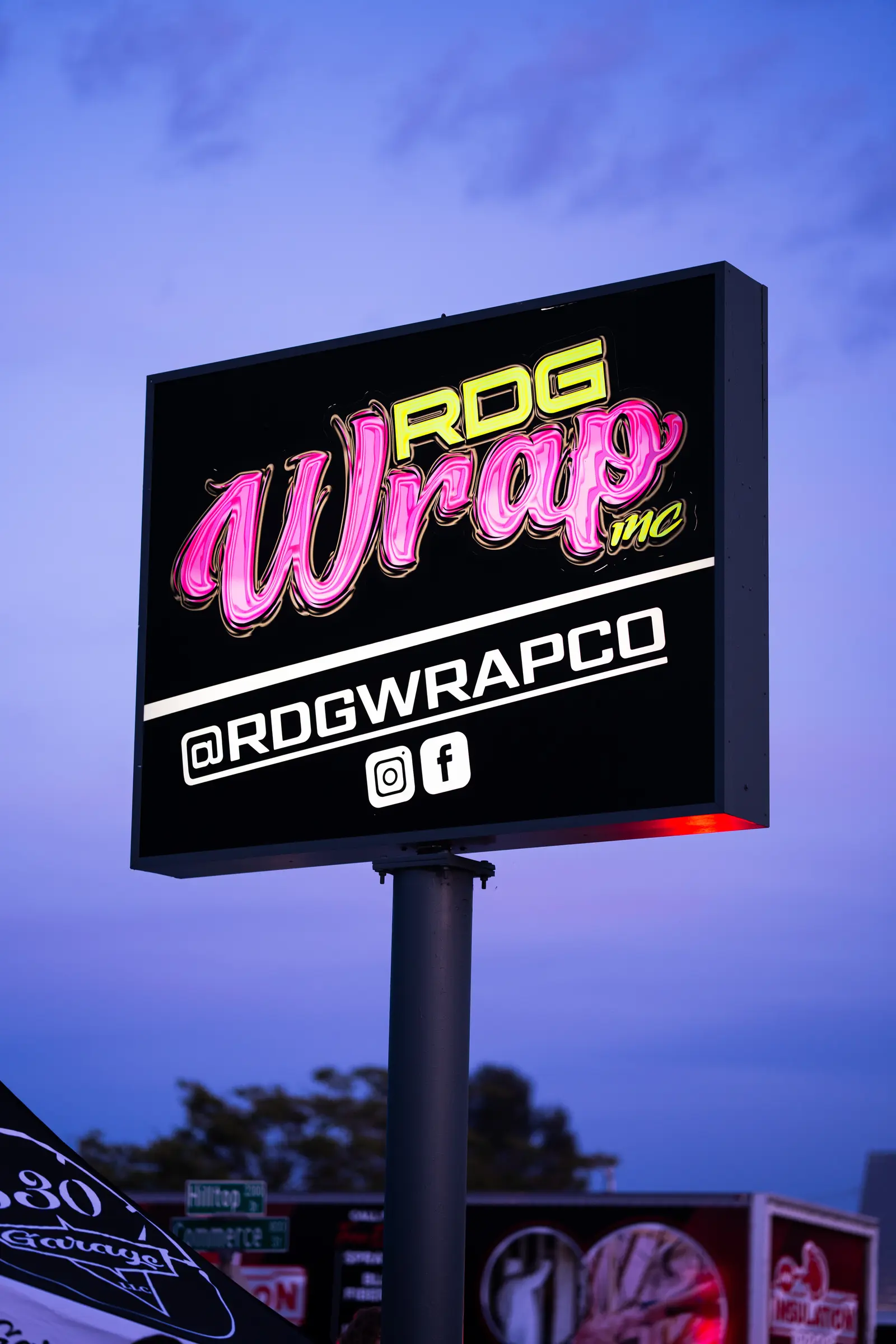 The lit RDG Wrap sign outside the Hilltop Drive shop at dusk