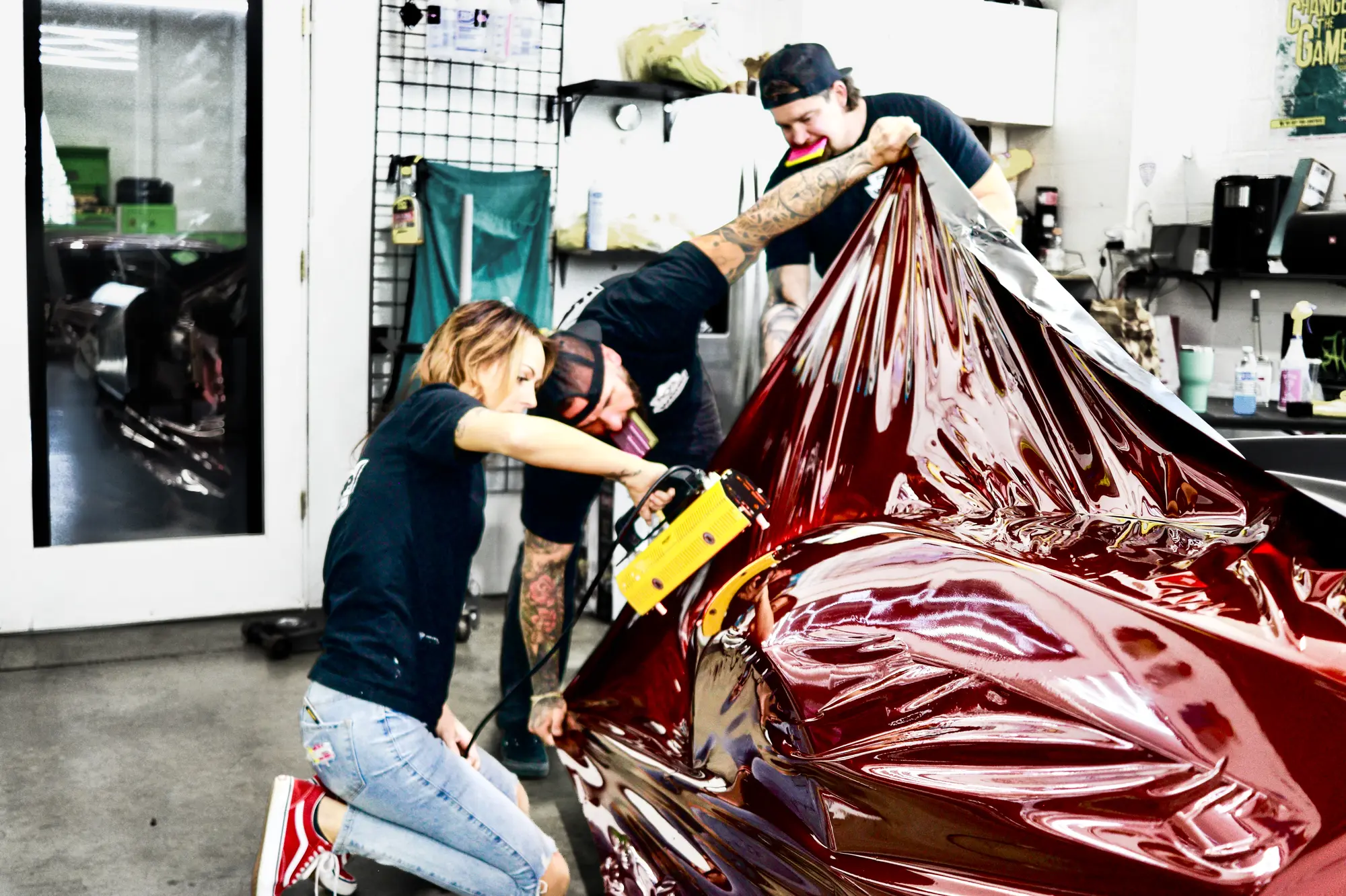 Installers stretching red chrome vinyl over a car in the shop
